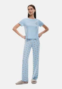 Lichtblauw T-shirt met korte mouwen met een koekje graphic, gecombineerd met bijpassende blauwe pyjamabroek met een cirkelvormig koekjespatroon, en grijze slippers.