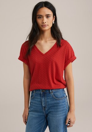 Red V-neck top with short rolled sleeves, featuring a textured zigzag pattern, paired with high-waisted blue denim jeans.