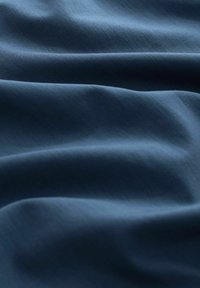 Tissu doux bleu foncé avec des plis délicats et une texture subtile créant un motif lisse et fluide.