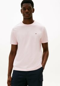 Jasnoróżowa bawełniana koszulka z okrągłym dekoltem i krótkimi rękawami. Posiada małe logo na lewej piersi. Gładka faktura.