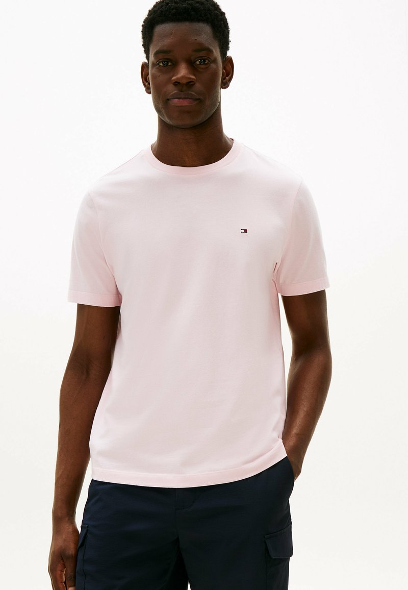 Jasnoróżowa bawełniana koszulka z okrągłym dekoltem i krótkimi rękawami. Posiada małe logo na lewej piersi. Gładka faktura.