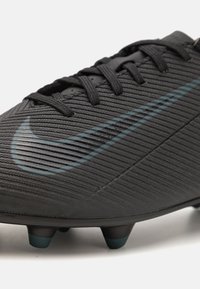 Crampon de football Nike noire avec surface texturée, arborant un logo swoosh proéminent en vert foncé et des crampons en caoutchouc coniques pour une meilleure traction.
