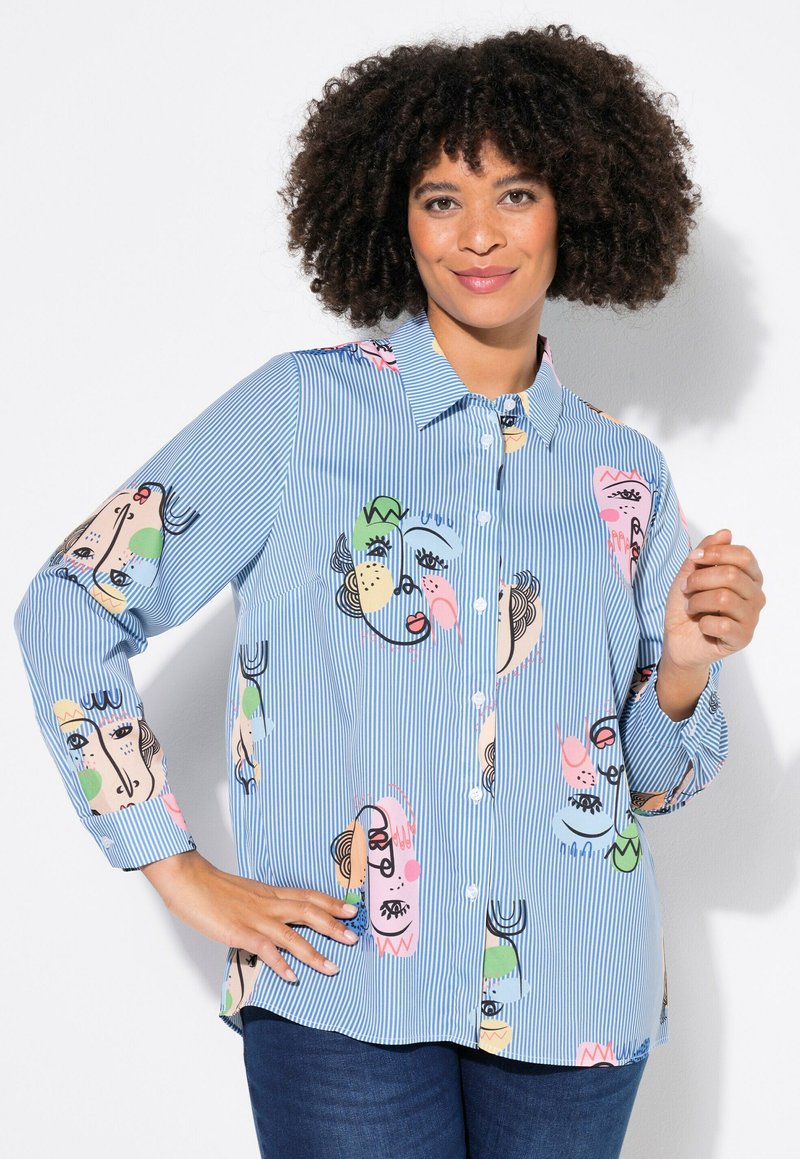 Camisa de botones a rayas azules con patrones de rostros abstractos en rosa, verde y negro. Tejido suave con mangas largas y cuello clásico.