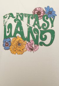 Světle barevné tričko s textem "FANTASY LAND" v zelené barvě s opotřebovanou texturou, doplněné o barevné květinové ilustrace.