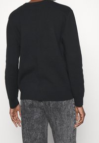 Czarny sweter dzianinowy z długimi rękawami, okrągłym dekoltem i prostym szwem na plecach. Noszony ze szarymi, spranymi dżinsami.