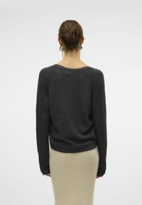 Pull en tricot gris foncé avec un col rond et des manches longues, présentant une coupe légèrement ample et un ourlet côtelé, associé à une jupe beige clair.