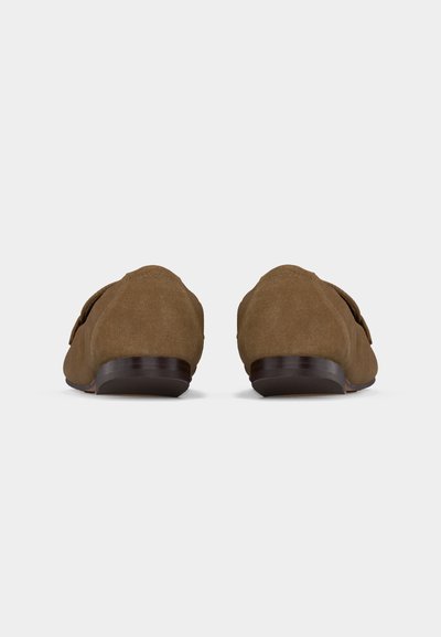 Ζευγάρι καφέ σουέτ μοκασίνια με χαμηλά σκούρα ξύλινα τακούνια, απεικονιζόμενα από πίσω σε απλό φωτεινό φόντο.