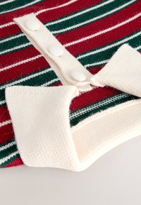 Pull en maille rayé rouge et vert avec un col crème et une patte de boutonnage. Les boutons sont texturés et assortis au matériau du col.