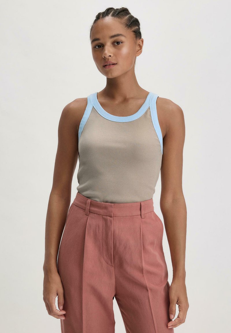 Beige gerippter Tanktop mit hellblauen Akzenten, kombiniert mit hochtaillierten rosa Hosen mit vorderen Falten und Seitentaschen.