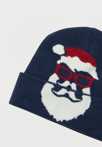 Marineblå strikket hue med et hvidt Santa-ansigt iført røde briller og en rød julestridshue med en hvid pom-pom.