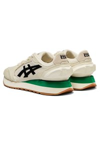 Béžové tenisky se zelenou a bílou podešví, s texturovanou špičkou, černým logem a prošívanými detaily na plátěném svršku.