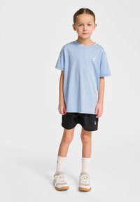 Ljusblå oversized t-shirt, korta svarta shorts, vita ankle-sockor och sneakers med grå accenter. Har logotyp på t-shirten och shortsen.