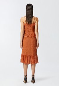 Abito arancione plissettato con accenti in pizzo, spalline a spaghetti e orlo in pizzo a strati. Texture liscia con silhouette aderente.
