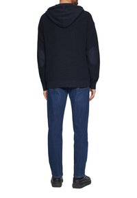 Donkerblauwe hoodie met een textuur gebreid ontwerp, met elleboogpatches en een relaxte pasvorm, gecombineerd met donkerblauwe jeans en zwarte schoenen.