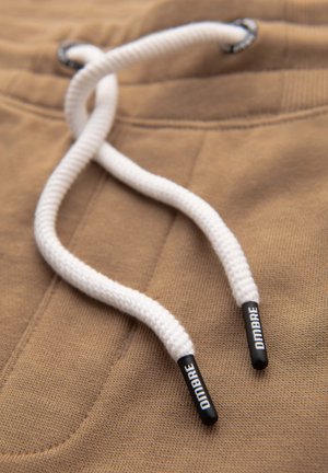 Tessuto marrone con una superficie texture presenta corde di chiusura bianche. Le estremità delle corde di chiusura sono in plastica nera con il testo "DIDAMBRE".