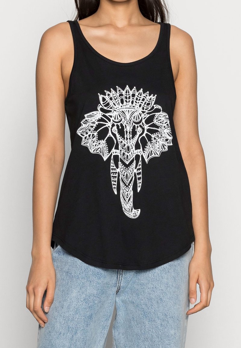Femme portant un débardeur noir avec un grand motif blanc orné de tête d’éléphant, assorti à un jean bleu clair, haut du corps visible.