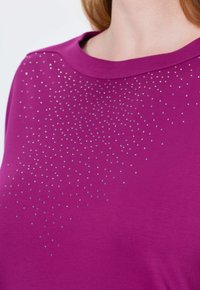 Fuchsia T-shirt met een ronde halslijn, voorzien van een verloop van zilveren rhinestones over de borst in een sprankelend patroon. Zachte stoftextuur.