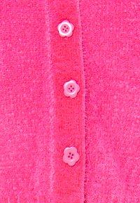 Fuchsia cardigan van een textuurstof. Voorzien van bloemvormige knopen in bijpassende tinten, die de details van de voorkant accentueren.