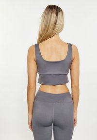 Harmaa urheilullinen crop-top, jossa on leveät hihnat, sileä pinta ja tiukka malli, yhdistettynä yhteensopiviin korkeavyötäröisiin leggins-housuihin.