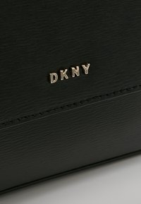 Borsa in pelle nera texturizzata con logo DKNY dorato. Il design presenta cuciture lisce e una forma rettangolare pulita.