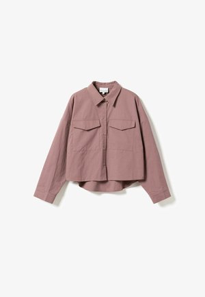 Trumpas marskinėlis dulkėtai rožinės spalvos, pagamintas iš lygaus audinio. Yra su smailiu apykakle, mygtukais priekyje, dviem krūtinės kišenėmis ir ilgomis rankovėmis su mygtukais ant riešų.