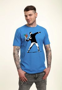 Modré bavlněné tričko s grafikou ve stylu graffiti, zobrazující postavu házející kytici, s černými a červenými akcenty.