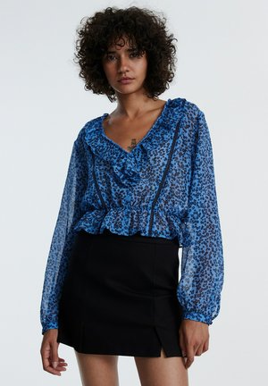 Transparente blaue Bluse mit schwarzem Blumenmuster, gerafftem Kragen und Ärmeln, kombiniert mit einem schwarzen Rock mit seitlichem Schlitz.