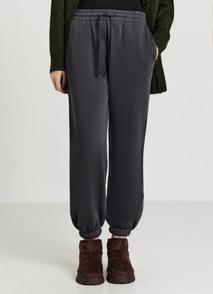 Pantalons de survêtement gris foncé avec une taille élastique, des poches latérales et des poignets froncés, associés à des bottes à la cheville marron. Texture lisse.