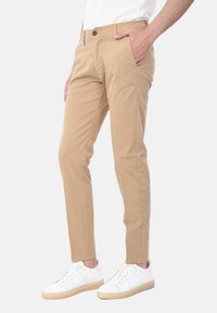 Chinos khaki con vestibilità slim, con tasche laterali, chiusura a bottone e tessuto di cotone morbido, abbinati a sneaker bianche.