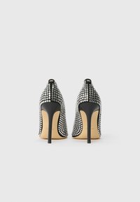 Black high-heeled shoes covered in rhinestones, featuring a pointed toe and a slim stiletto heel. Smooth interior with a gold sole.