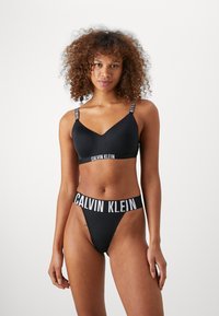 Crni bikini set s V-izrezom grudnjaka s podesivim remenima i odgovarajućim tangama, oboje s bijelim natpisom "Calvin Klein".