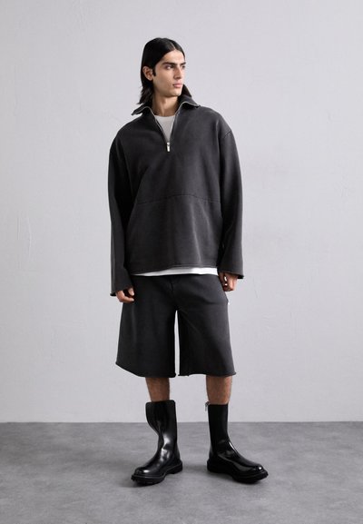 Mørkegrå fleece-pullover med halvlukking, parret med matchende shorts og blanke svarte ankelstøvler. Enkelt design med minimale detaljer.