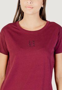 T-shirt in cotone bordeaux con maniche corte e scollatura rotonda, caratterizzato da un logo testurizzato con applicazioni di strass al centro.
