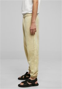 Lys beige joggebukser med snøring i livet, ribbestrikkede ankler og en myk tekstur, kombinert med svarte stroppesandaler for kontrast.