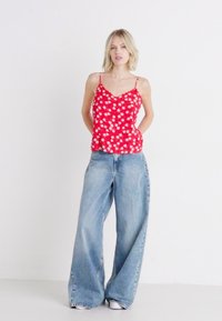 Canotta con stampa floreale rossa e spalline sottili, abbinata a jeans a gamba larga blu chiaro e sneakers bianche. Tessuto morbido e vestibilità rilassata.