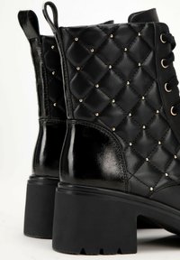 Black ankle boots with a quilted design, adorned with gold studs, featuring a glossy finish and a thick, textured rubber sole.