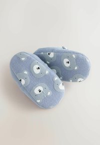 Pantofole azzurro chiaro con una texture morbida, caratterizzate da un motivo a orso in grigio e bianco. Forma arrotondata con un piccolo tacco e bordi cuciti.