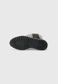 Semelle de botte noire avec un motif de grip texturé, présentant des crêtes et des rainures pour une traction, sur un fond blanc uni.