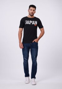 Svart t-skjorte med "JAPAN" trykt i fete, slitte hvite bokstaver. Bæres med blå slitte jeans og hvite joggesko.