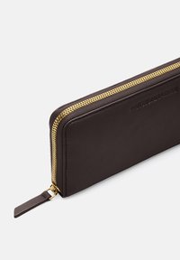 Brown leather wallet with a gold zipper, featuring a rectangular shape and textured surface. Brand name embossed on one side.
