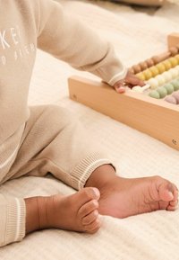 Ensemble en tricot beige avec des poignets côtelés, un boulier en bois avec des perles pastel, et une légère couverture texturée en dessous.