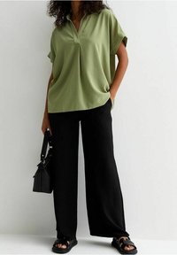 Light green, short-sleeve top with a textured pattern, paired with black, wide-leg trousers and black sandals, carrying a black handbag.