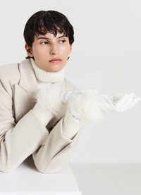 Gants blancs avec des poignets en fourrure douce, assortis à un col roulé blanc côtelé et un manteau beige clair. Design simple et élégant avec des textures douces.