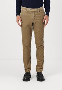 Pantalons en velours côtelé tan avec une coupe droite, dotés d'un bouton et de passants de ceinture. Portés avec des chaussures noires.