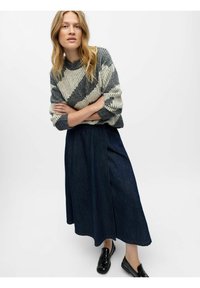 Pull en maille rayé confortable en gris et crème, associé à une jupe maxi en denim foncé. La tenue présente une coupe décontractée et de simples chaussures noires.