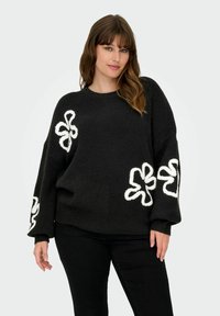 Zwarte gebreide trui met witte bloemenborduursels op de mouwen. Heeft een losse pasvorm, ronde halslijn en een textuurstof.