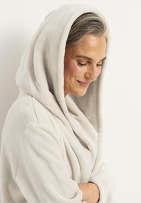 Ljust grå hoodie-robe i mjukt, plyschmaterial, med en avslappnad passform och vida ärmar, som har en slät textur och inga synliga mönster.