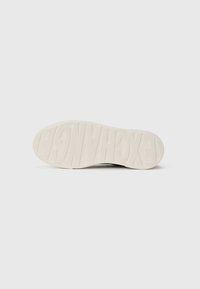Semelle d'une sneaker blanche avec le nom de la marque "EXCHANGE" embossé en grandes lettres sur le fond blanc uni.