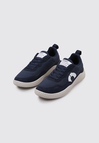 Baskets bleu marine en matériau synthétique avec une semelle texturée, comportant un logo et une étiquette blancs sur la languette, et un design à lacets.