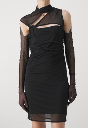 Czarna sukienka bez rękawów z przezroczystymi siateczkowymi długimi rękawami, wysokim kołnierzem i asymetrycznymi wycięciami na piersiach i ramionach.